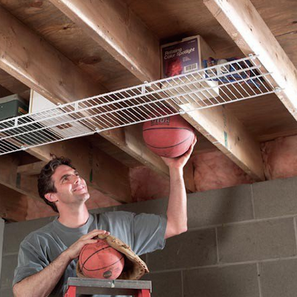 A man stores basketballs in an overhead attic shelf.