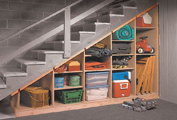 Storage built under a set of basement stairs is filled with various household items like sleeping bags, Tupperware, coolers and riding toys.