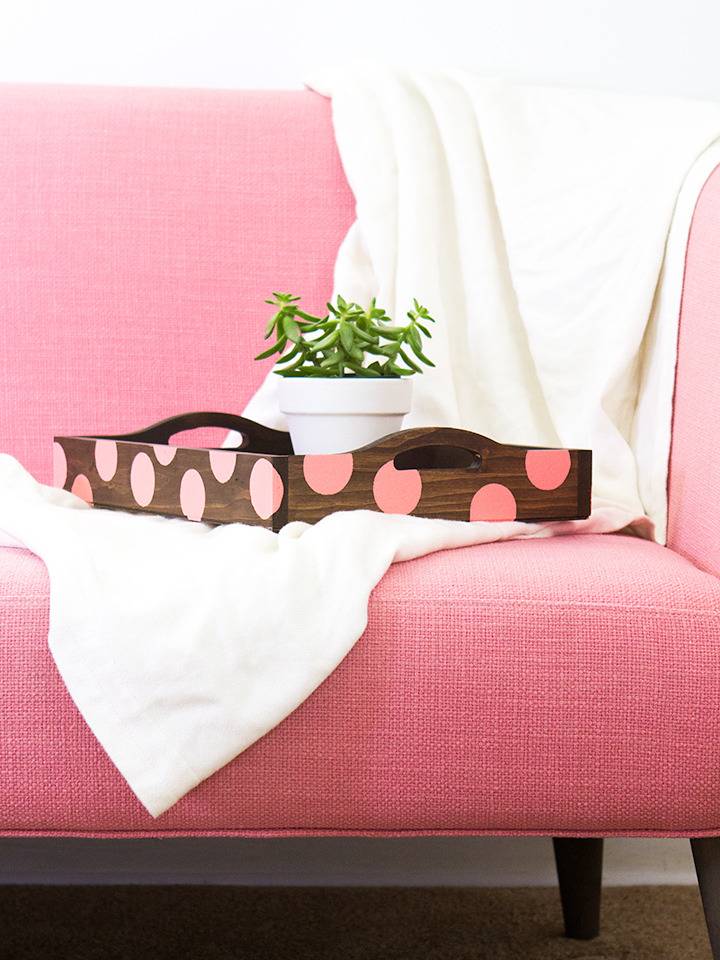 A pink and brown serving tray sits on top of a hot pink ottoman in a pink room.