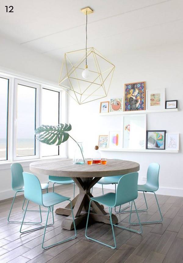 Round dinning table with six blue color chairs, some drinks at the top, shandler is hanging on the top, and some photo frames on the wall in a dinning room.