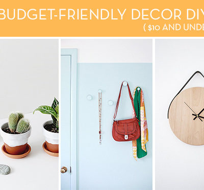 A gold spritzer can next to two potted plants and two rocks, a brown purse and colored scarf hanging on a blue wall and a wooden round clock with no numbers.