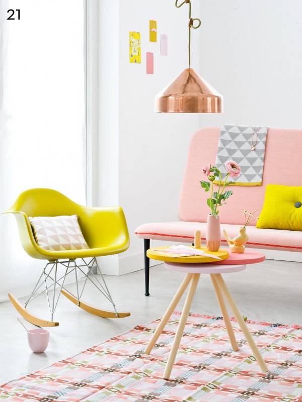 Pink sofa and mustard color rocking chair and mini round table with flower vase at top and hanging light in pastel room.