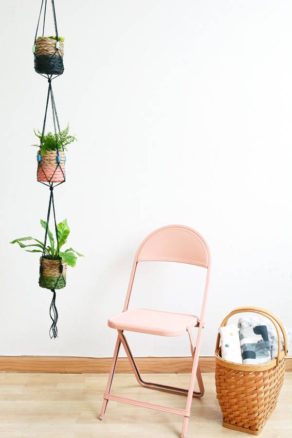 Plants are growing in a vertical hanger near a pink folding chair.