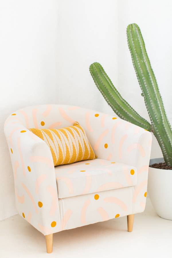 A yellow and white chair is near a cactus growing in a white container.