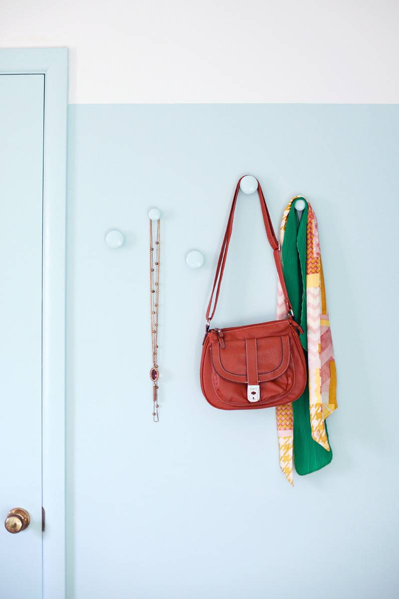 A purse and jacket are hanging on a white wall near a door.