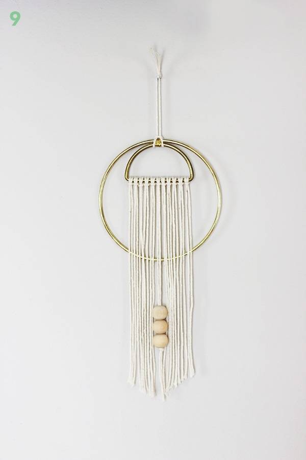 A brass circle and a brass half circle with string folded over the flat part are hanging on a white wall.