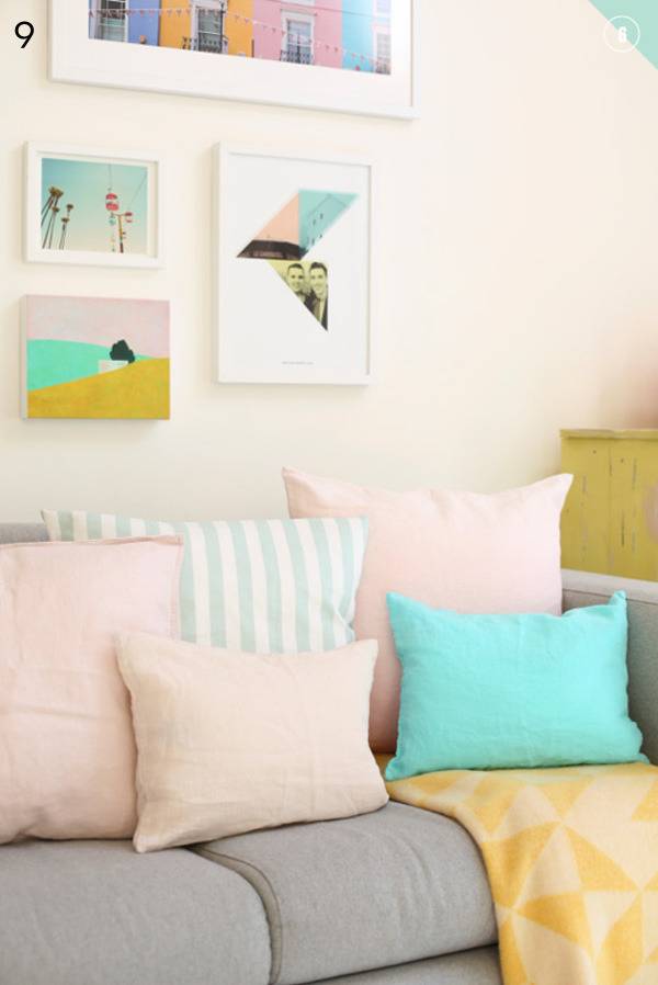 Pastel colored pillows on top of a grey couch with framed artwork hanging on the wall above it.