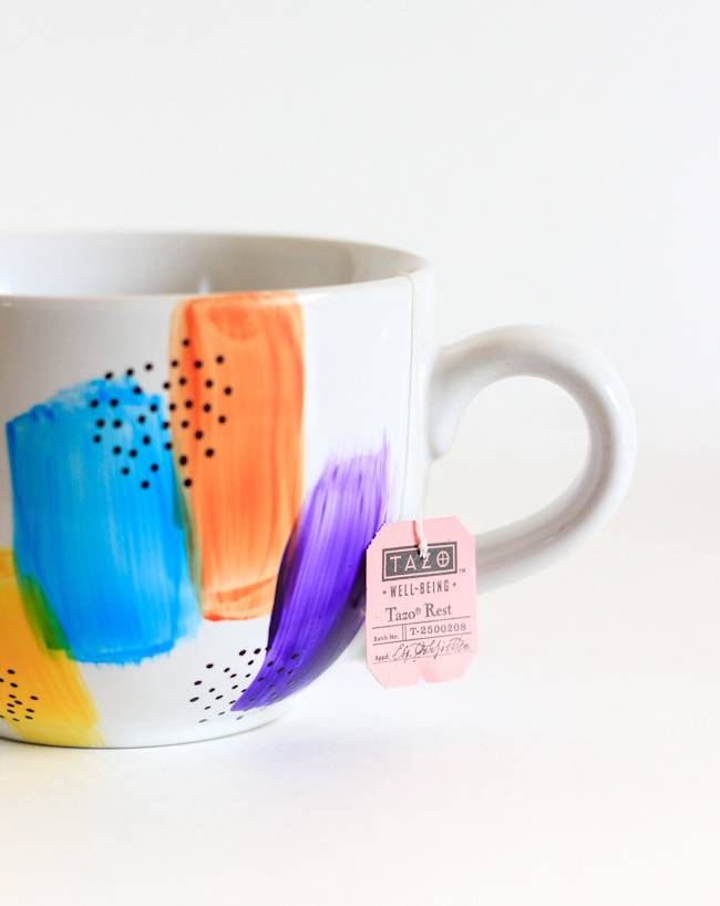 White mug with tag on handle, decorated with swatches of different bright colors and tiny dots.