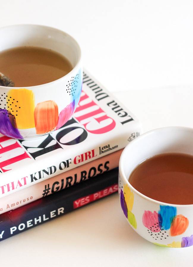 Two cups of coffed in brightly painted small cups with one cup on top of three stacked books.