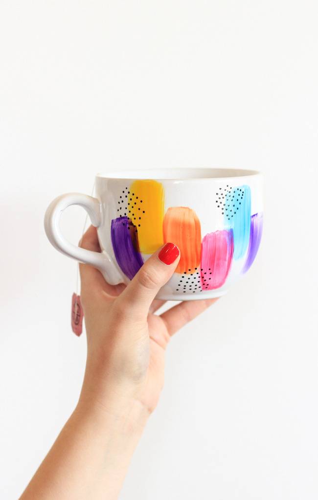 A woman's hand holding a colorfully painted coffee mug.