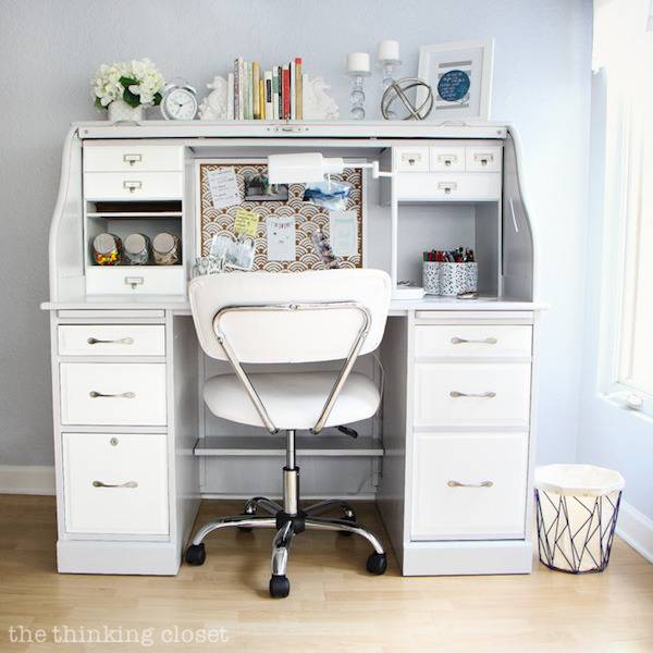 A white desk with a chair seated at it in a room with a window.
