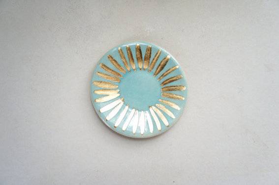 A teal plate with gold stripes made to resemble the sun is hung on the wall.
