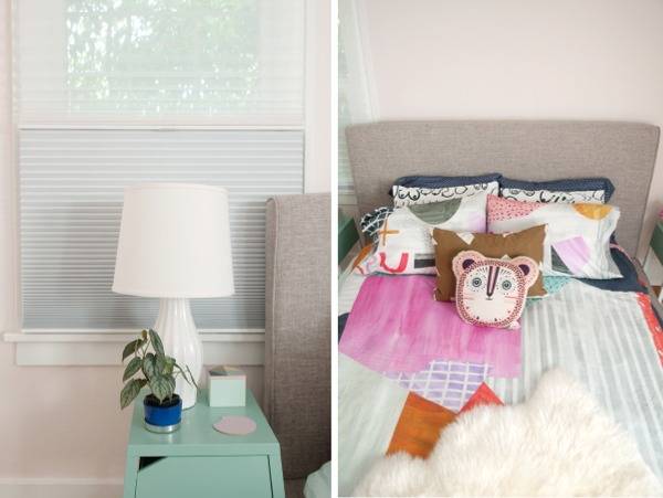 A cute teal bedside table has a white lamp in front of a window, and a bed has an animal pillow stacked on top of other break pillows and bedspreads.