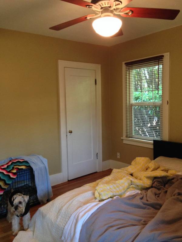 The light is on in a ceiling fan above a slopilly made bed.