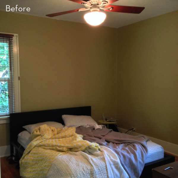 A messy unmade bed sits under a ceiling fan in a yellow room.