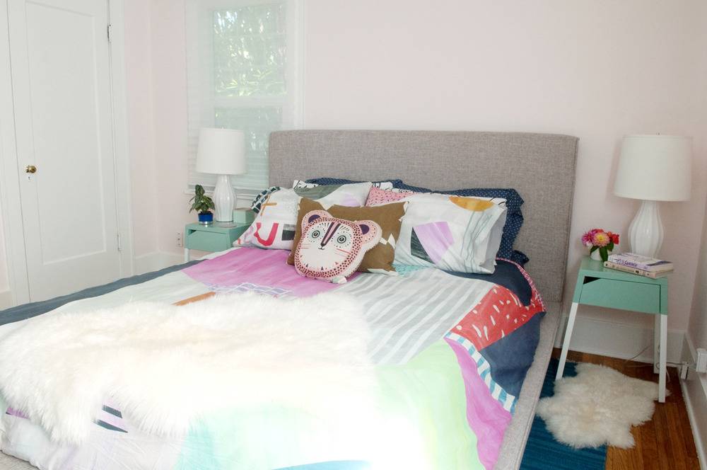 A bed with a grey fabric headboard has colorful pillows and one pillow on the top shaped like an animal head.