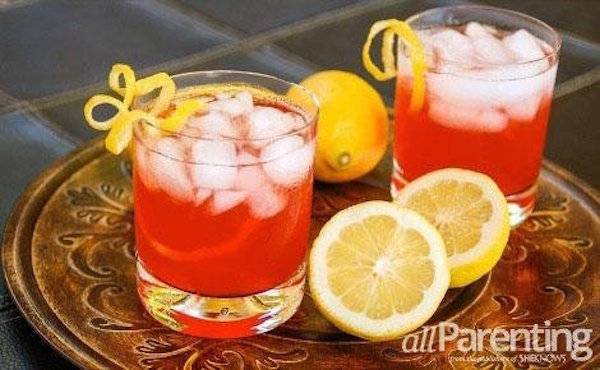 Two reddish colored drinks are served on a copper tray with lemons.