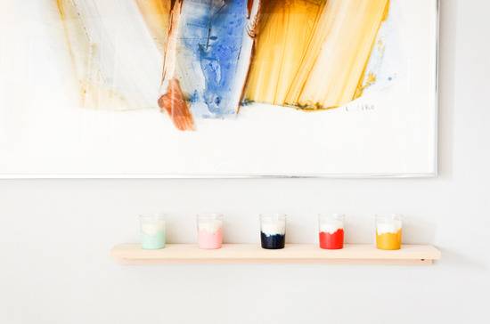 A shelf with colorful candles on it is underneath a large colorful picture.