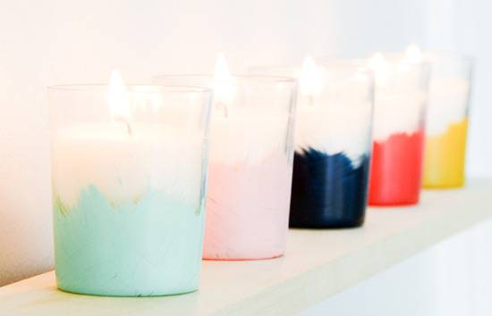 Several lit multicolored candles are in a line on a mantle.