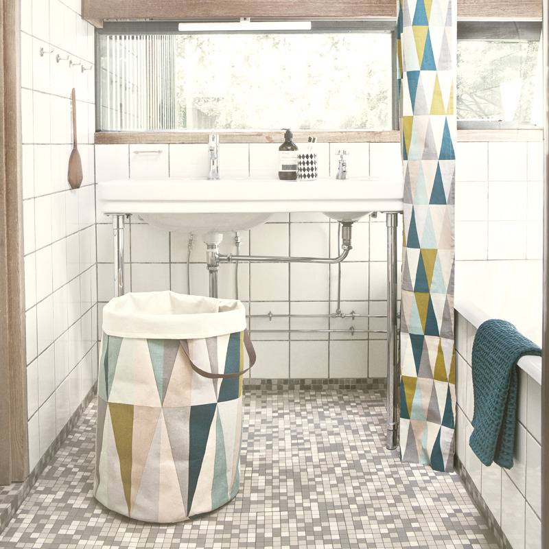 A white sink and tub are accented by a shower curtain and trashcan in a bathroom.