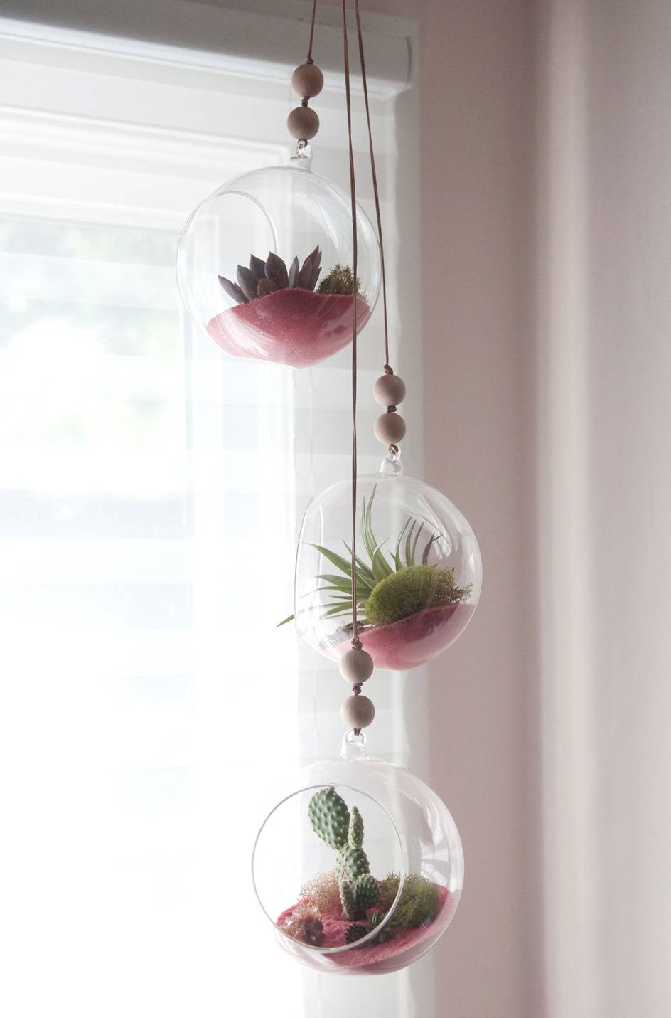 A three hanging glass plant pots near the window