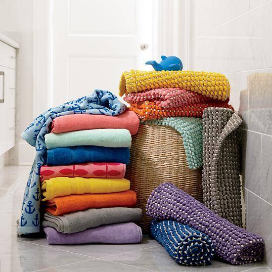A stack of colorful towels sits on the floor next to towels rolled up on top of a hamper.