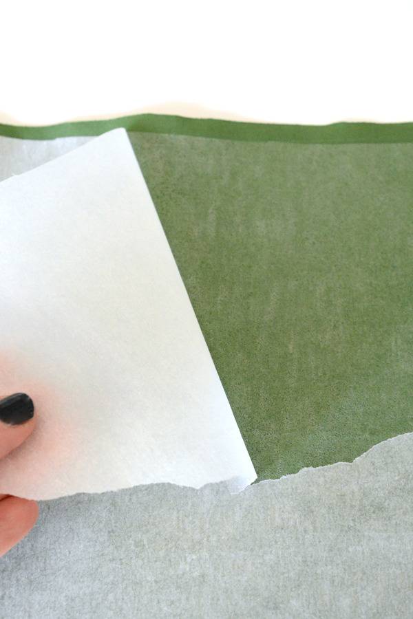 A person peels white paper backing off of a green sticker.