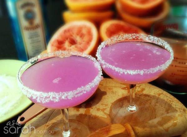 Two margarita glasses are filled with pink drinks with sugar rimming the edges of the glass.