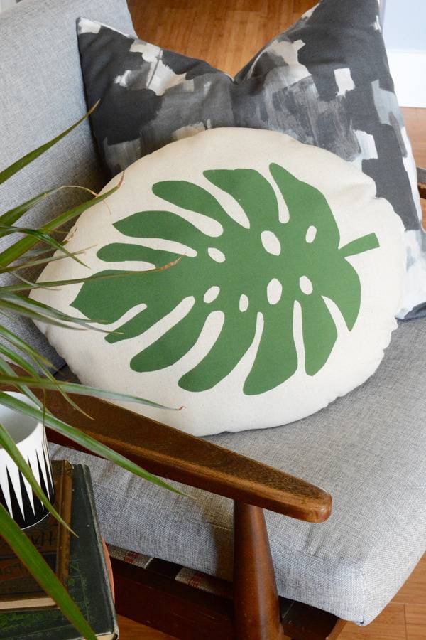 An oval shaped pillow with a leaf on it sits on a mid-century modern chair.