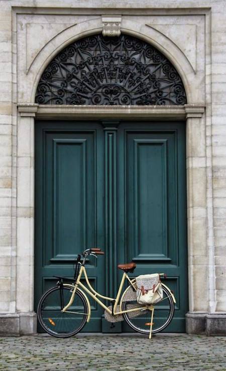 A bike is parked in the door frame of a large double door that is green.