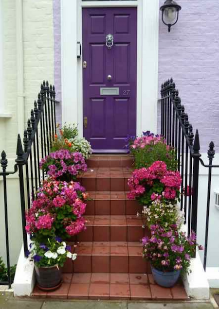 Red brick steps with potted flowers on both sides leading up to a purple door.