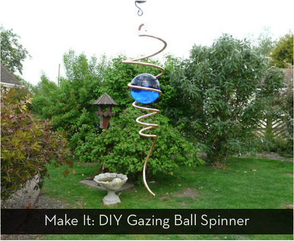 A very tall swirly brass ball spinner with a blue ball in the middle is on a lawn next to a bird bath.