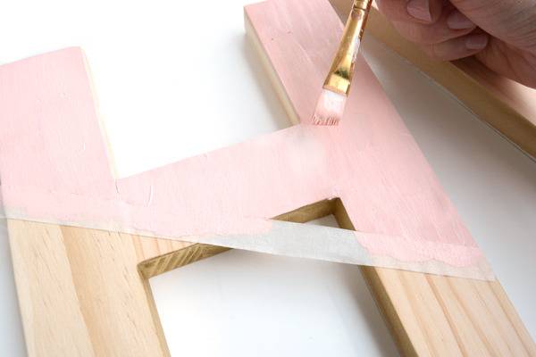 A person is painting a wooden letter H.