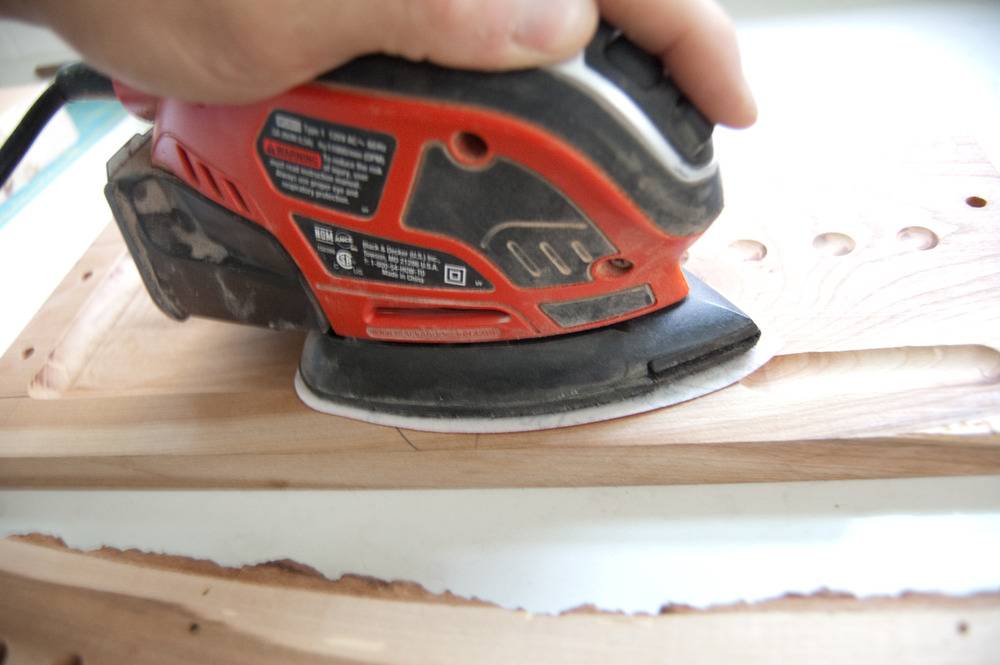 A man uses a hand sander to sand a wood cutting board.