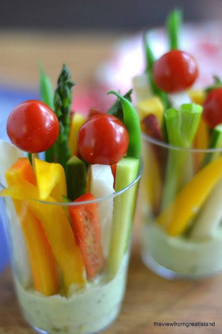 A variety of veggies are sitting in clear cups with ranch at the bottom.
