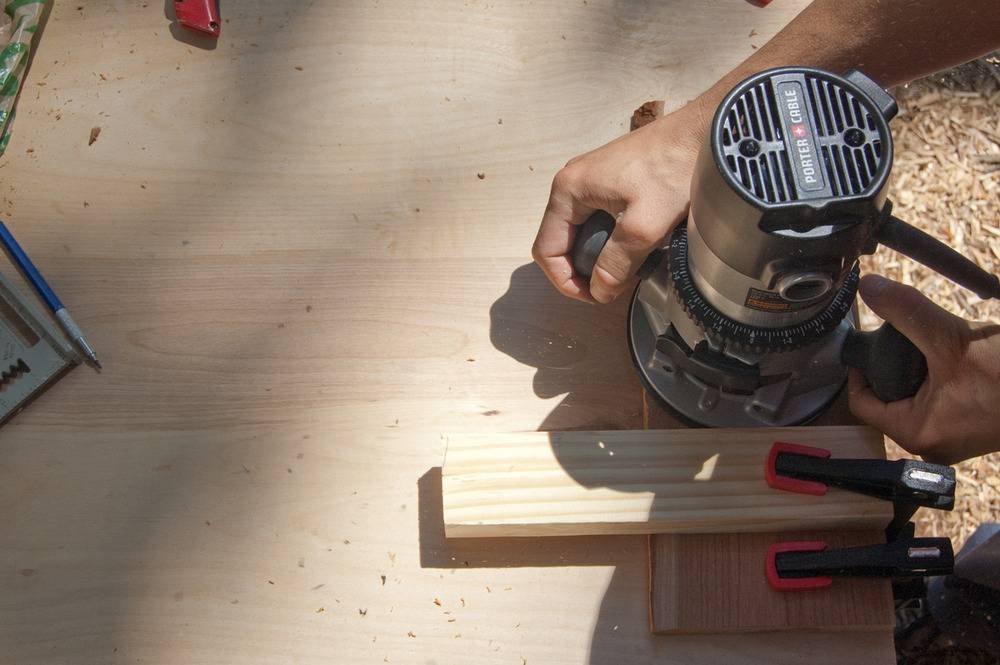 Man sanding a piece of wood outdoors using a power sander.