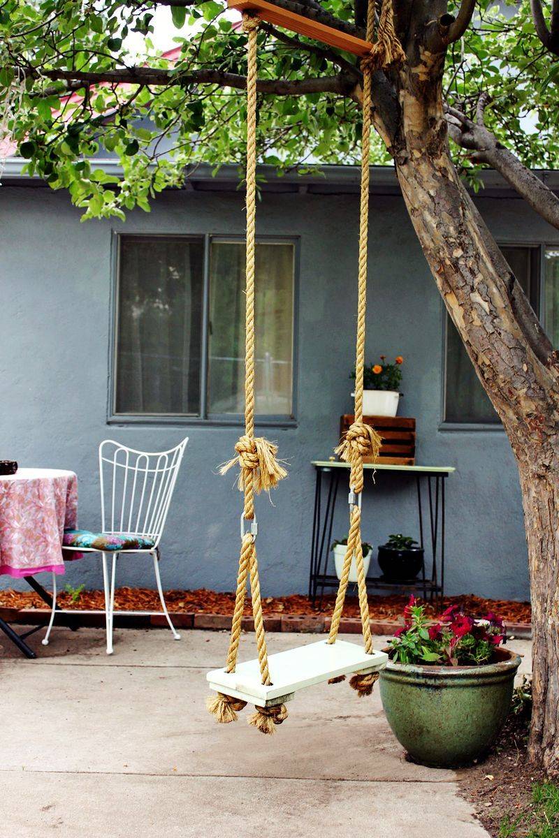 A backyard swing hanging from a tree next to a green planter.