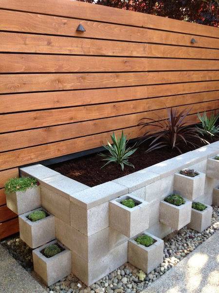 Concrete planter pots jut out of a large concrete planter on a patio.