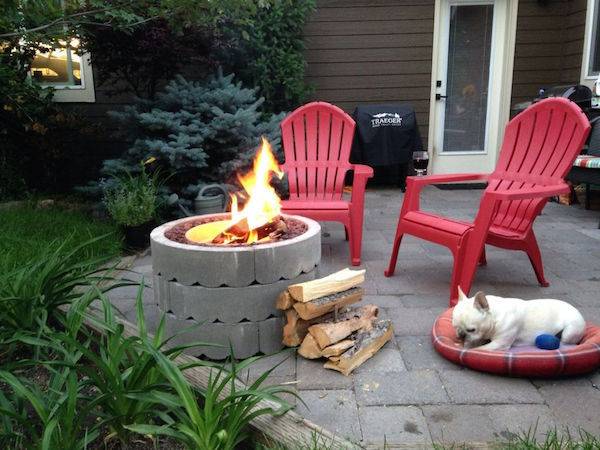 Red chairs and a dog around a fire pit.