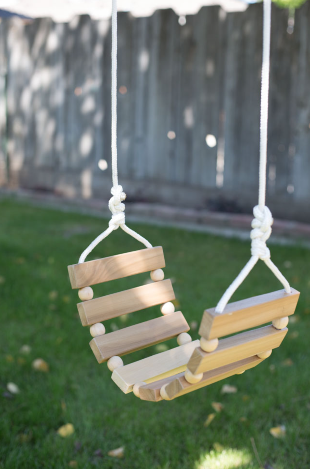 Wood slats are strung with fabric to create a tree swing over a lush lawn.