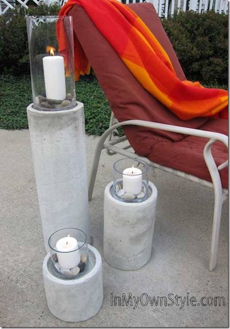 Three ascending hurricane candles outside on pavement next to a lounge chair with a red cushion and orange towel on it.