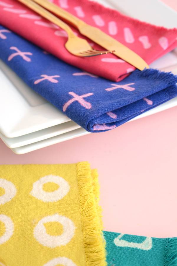 A gold fork and knife sitting top of a red and pink folded napkin which sits on top of a blue and ping folded napkin which is sitting on three white plates behind a yellow piece of cloth with white circles on it.