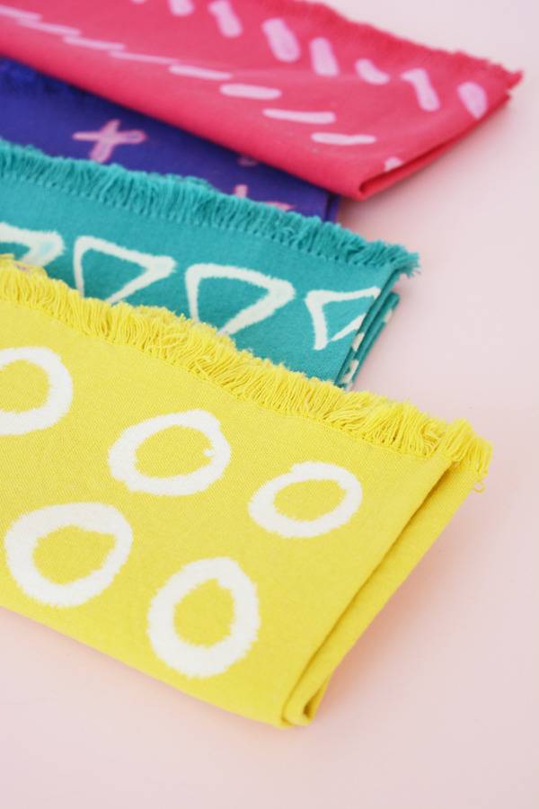Geometric shapes are painted on pink, blue, teal, and yellow napkins.