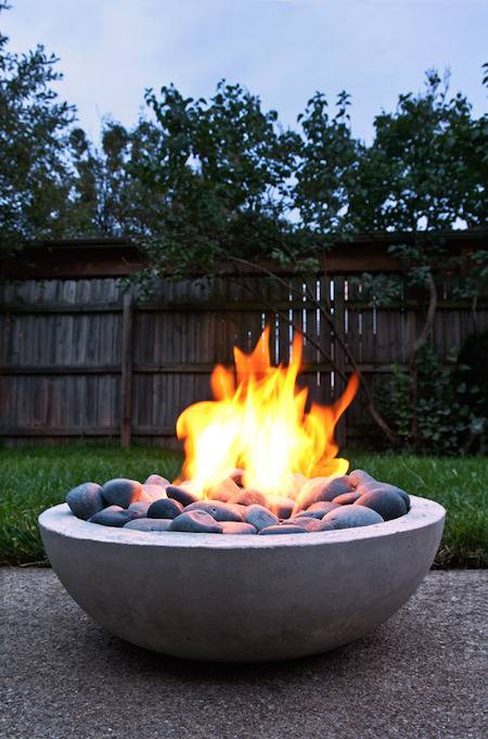 A round outdoor stone fire pit with round rocks in it is lit with a big fire.
