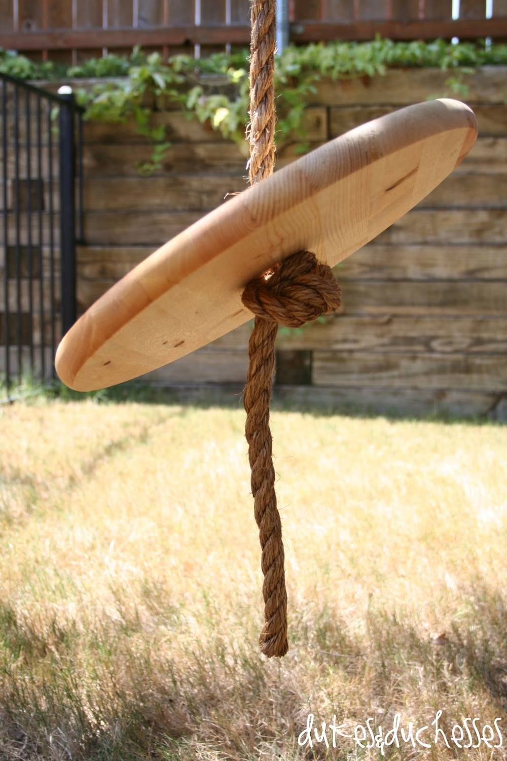 A round wooden disk of a swing is hanging from a rope.