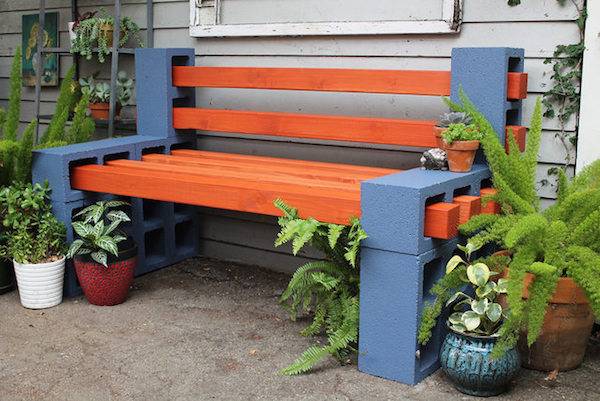 A bench made from blue cinderblocks and red boards surrounded by plants.