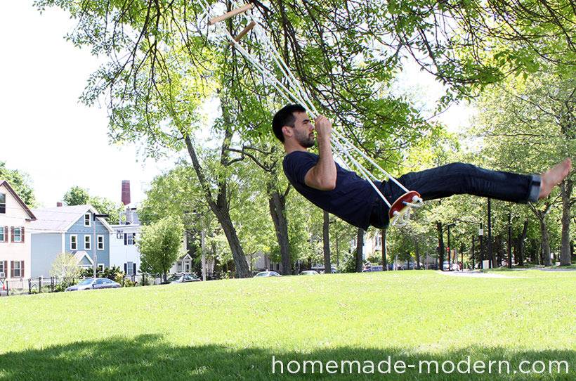 A man wearing dark colors is swinging on a swing in a tree.