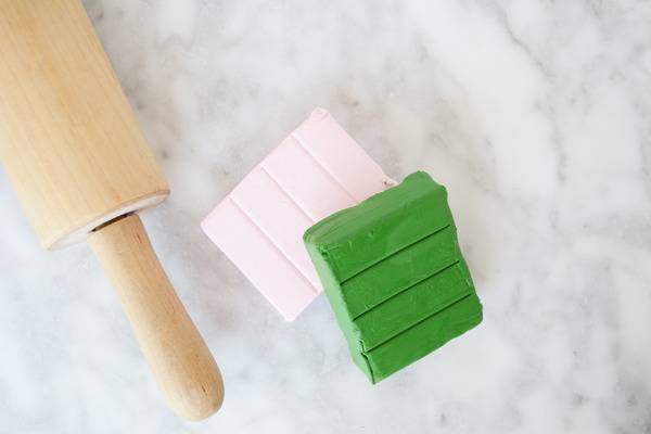 Wooden rolling pin on top of a marble counter next to pink and green clay.