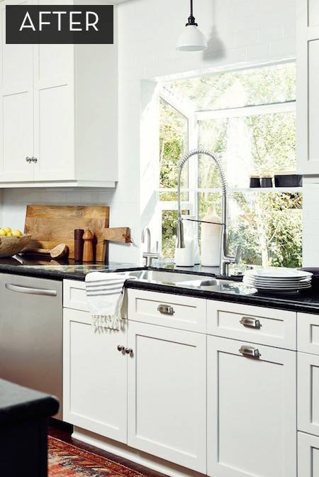 A white kitchen with black countertops, a no touch faucet and a bay window behind the sink.