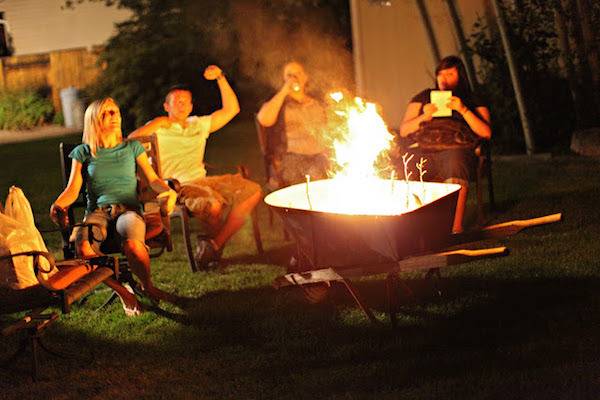 People sitting around a backyard fire pit with yellow flames coming out of it.